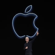 L'homme, sur scène, fait un signe de paix avec les doigts devant un logo d'Apple sur fond noir.