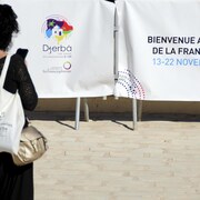 Une participante se tient devant des banderoles annonçant le 18e Sommet de la Francophonie à Djerba, en Tunisie.