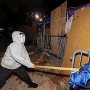 Un manifestant masqué frappe à coups de bâton sur une clôture de sécurité.