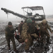 Des soldats transportent un blessé dans un terrain vague enneigé. 