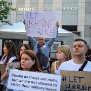 Des manifestants sont rassemblés devant l'ambassade avec des pancartes dans les mains.