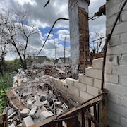 Les ruines d'une maison avec des arbres et d'autres maisons endommagées à l'arrière.