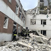 Trois secouristes s'apprêtent à entrer dans un immeuble lourdement bombardé au milieu de décombres.