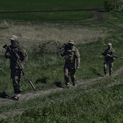 Des soldats ukrainiens munis d'armes de précision marchent sur un chemin de terre.