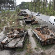 Des tanks détruits et carbonisés en bordure d'une route. 
