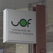 Affiche près d'un immeuble sur lequel on peut lire UOF, université de l'Ontario français. 