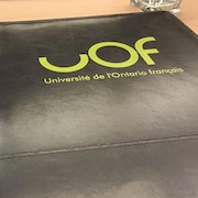 Un bloc-notes noir avec le logo de l'UOF est posé sur un bureau.