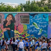 Un rassemblement de plusieurs dizaines de personnes devant une murale qui représente deux fillettes.