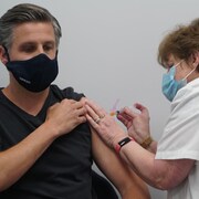 Un homme se fait injecter un vaccin contre la COVID-19 dans l'épaule.