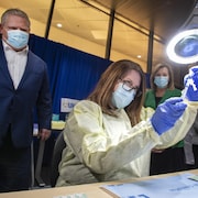 Une technicienne remplit une seringue du vaccin contre la COVID-19 sous le regard du premier ministre Doug Ford.