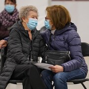 Deux dames assises tout près l'un de l'autre sur des chaises dans le centre sportif à Louiseville, le 25 mars 2021.