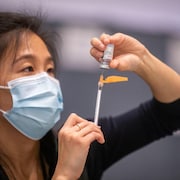 Une femme qui porte le masque sanitaire prépare un vaccin.