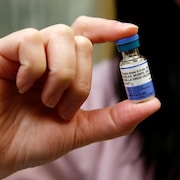 Une fiole de vaccin contre la rougeole tenue entre le pouce et l'index de la main.