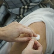 Un travailleur de la santé applique de la ouate et un pansement sur le bras d'une patiente âgée venant tout juste de recevoir son vaccin.