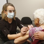 Une femme portant un masque et une visière administre un vaccin à une femme âgée. 