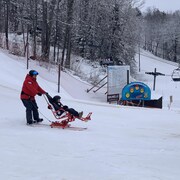 Un moniteur en ski et un enfant dans un siège adapté, sur la piste.