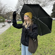Une femme regarde dans un téléphone avec des lunettes de protection, en tenant un parapluie.