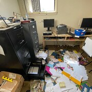 Un bureau saccagé avec des classeurs ouverts et des documents sur le sol.