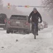 Un homme en vélo lors d'une tempête de neige printanière s'abat à Regina, en Saskatchewan, le 19 avril 2023.