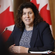 Karen Hogan parle au micro, assise à une table devant des drapeaux canadiens.