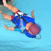 Un bébé flottant dans une piscine à l'aide d'une veste de flottaison.