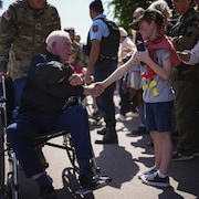 Un vieil homme en fauteuil roulant serre la main d'un jeune homme.