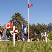 Des drapeaux canadiens déposés sur de petites croix blanches dans un cimetière.