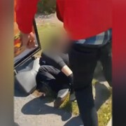 Une capture d'écran de la vidéo qui montre un adolescent se faire tabasser. Celui-ci est au sol. Un jeune portant un chandail rouge, poing demi-serré, se tient debout devant lui.