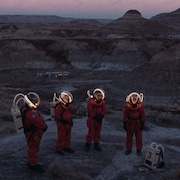 Quatre astronautes sont en demi-cercle dans une vallée ressemblant à un paysage de la planète Mars. 