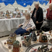 Des personnes âgées examinent un grand village de Noël miniature.