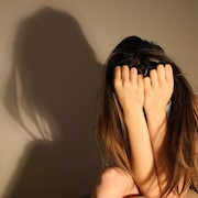 Une femme se couvre le visage dans un coin d'une pièce avec son ombre au dessus d'elle.