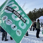 Un drapeau à l'effigie de plusieurs syndicats, avec plusieurs personnes en arrière-plan sur un sol enneigé.