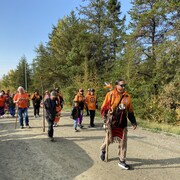 Une vingtaine de personnes marchent près d'une forêt.