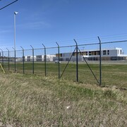 Photo extérieure de la prison d'Amos, à travers une clôture munie de barbelées.