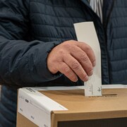 Un homme en train de déposer son bulletin de vote dans une boîte de scrutin.