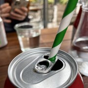 Vue rapprochée d'une table de restaurant sur laquelle est déposée une canette de boisson gazeuse qui contient une paille à rayures vertes et blanches.