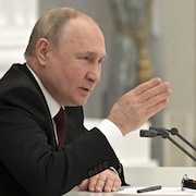 Vladimir Poutine, de profil, fait un geste de la main. 