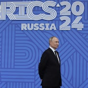 Vladimir Poutine sourit devant l'affiche du sommet.