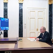Vladimir Poutine est assis à son bureau derrière un écran de visioconférence.