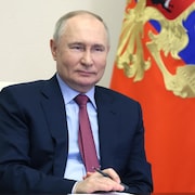 Vladimir Poutine assis devant un drapeau de la Russie.