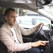 Un jeune homme porte des écouteurs en conduisant.