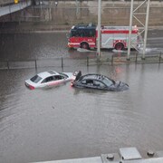 Deux voitures quasi submergées et un camion de pompiers dans la voie de l'autre côté d'un terre-plein.