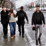 Des policiers et des enquêteurs escortent une personne en état d'arrestation.