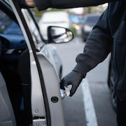 Gros plan sur la main d'un voleur en train d'ouvrir la portière d'une voiture.