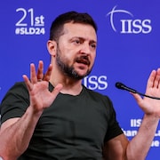 Volodymyr Zelensky parle dans un micro en bougeant les mains. 