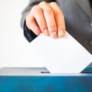 Une personne met une enveloppe dans une boîte de scrutin.