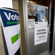 Un homme ouvre une porte où est posée une affiche disant qu'il s'agit d'un bureau de vote qui est ouvert de 8 à 20 heures.
