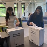 Deux jeunes élèves mettent des bulletins de vote dans les urnes.