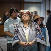 Maxwell Johnson et sa petite-fille portent un survêtement et une coiffe traditionnels et marchent, lui devant et elle derrière, vers l'endroit où va avoir lieu la conférence de presse.