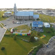 Vue aérienne des cabanes colorées des producteurs, sur un terrain vague à côté de l'église et d'un restaurant de Sainte-Luce.